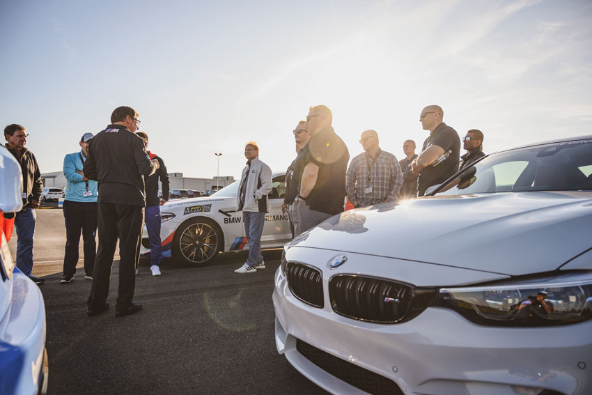 Mike D’Ambrosio captures a group of people standing between two white BMWs as they listen to a speaker on the track