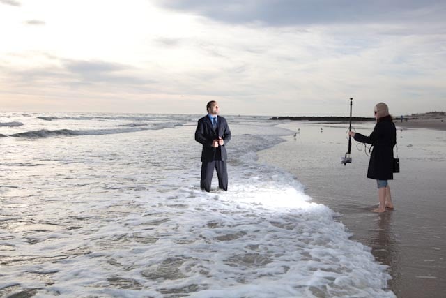 Behind the scenes from Jordan Hollender's shoot shows a man standing in the ocean in a suit being lit from the shoreline