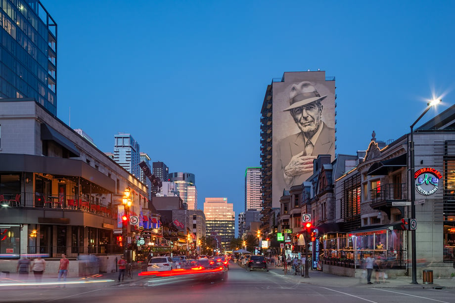 The mural of Leonard Cohen stands out against a busy street taken during blue hour