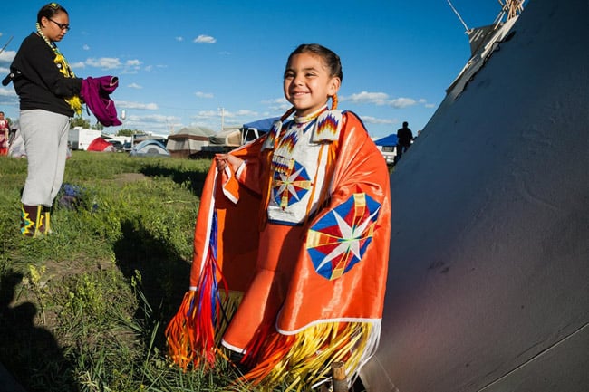 Native American child smiling, wearing colorful traditional clothing 