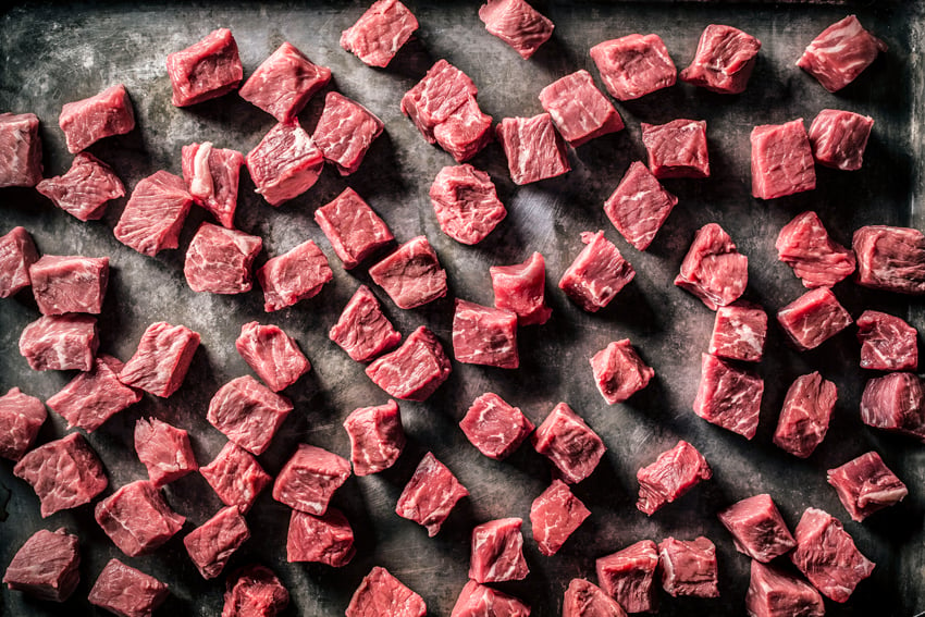 cubes of raw meat are lined on a black surface