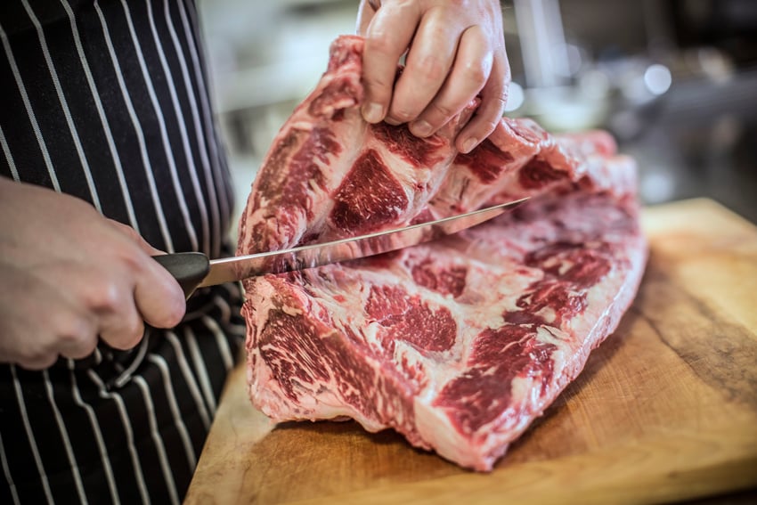 a large piece of red meat is cut into in a large knife