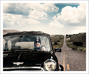 Image of a woman in glasses and a headscarf, driving a vintage Mini Cooper, photographed by Tarick Foteh