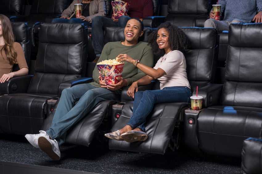 Photo for Cinemark of a couple sharing popcorn sitting luxury loungers.