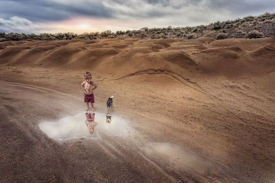 Photo of Ryatt and his wolf brother looking at their reflections in a puddle in the desert sand.