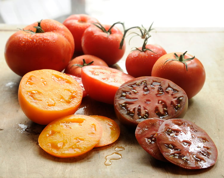 still life photography showing whole tomatoes beside sliced tomatoes, against a neutral background
