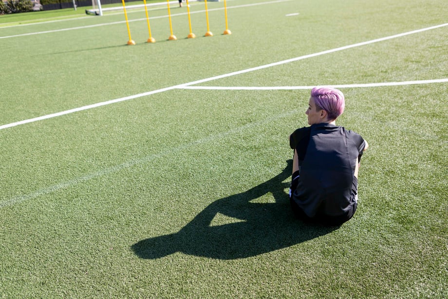 Sabrina Hill photographs Megan Rapinoe sitting on the green with her silhouette stretched out behind her in the late light for The Skills