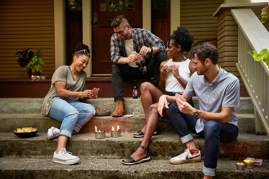 Group of friends play cards on porch surrounded by Nunya bonfire and beeswax candles shot by John Valls