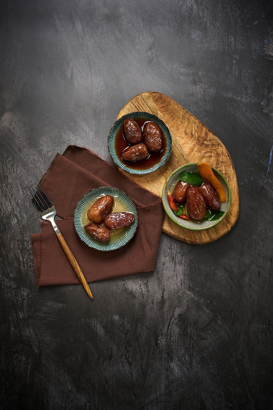 Three ceramic bowls of dates in syrup on top of a  wooden board with black backdrop shot by Rebecca Peloquin for the Los Angeles Times