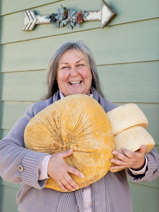 Woman happily holding three large wheels of cheese shot by Angela DeCenzo for National Geographic Traveller Food magazine