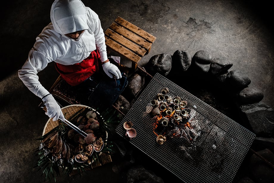 Okano Mitsue, age 75, grilling an assortment of shellfish at Ama Hut Hachiman in Toba, Mie Prefecture. Photographed by Ben Weller.