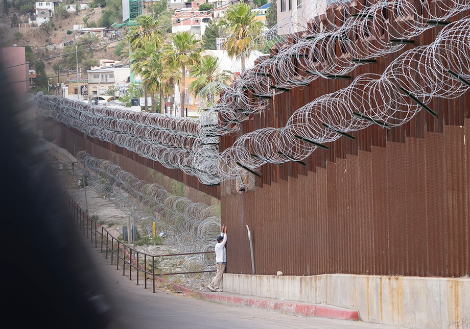 A man speaks to his family through the border wall in Nogales, Arizona. Photography by Bob Rives. 
