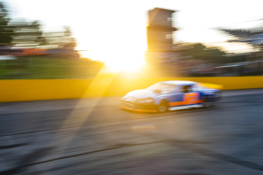 Race car zooms by the car at sunset at Wake County Speedway shot by Bryan Regan for Walter Magazine