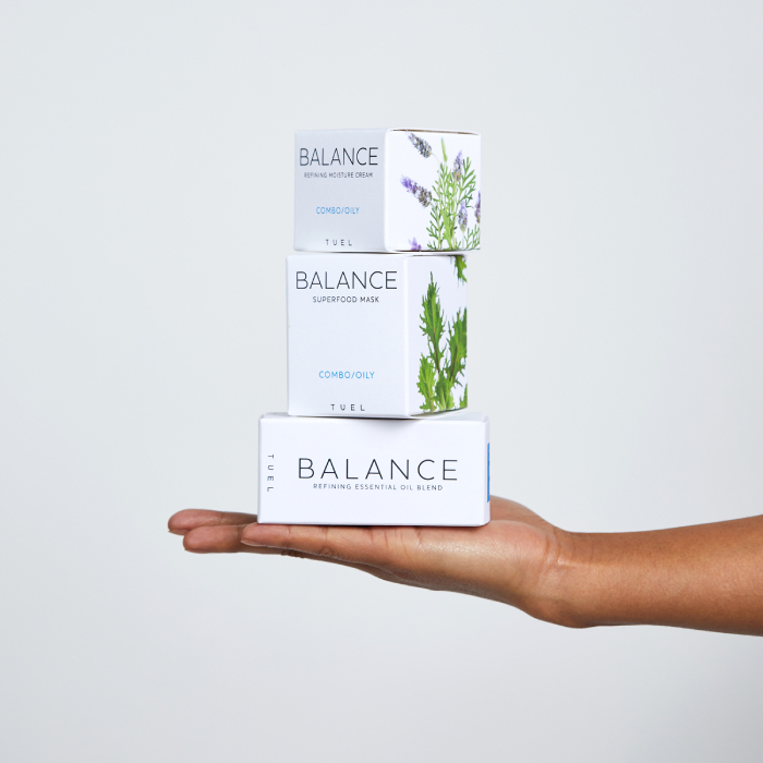 A hand holding three Tuel skincare products featuring Chava Oropesa's ingredient images on product packaging