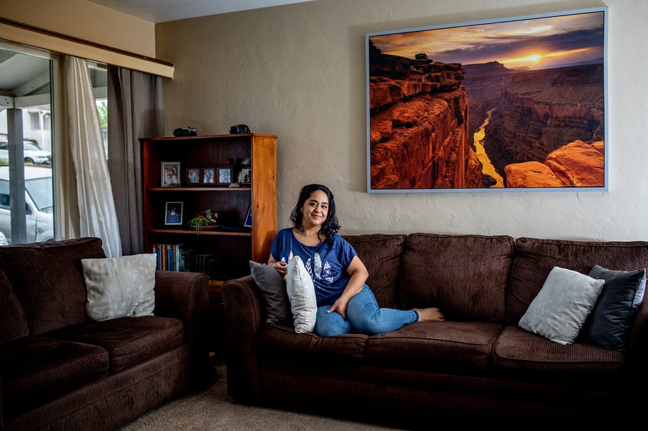 Woman sitting on her couch with giant grand canyon photo behind shot by Jaime Borschuk for Women at Home project