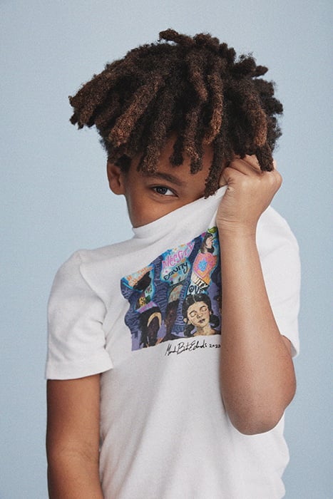 A young kid shyly holds up the collaborative t-shirt to his face. Photographed by Janelle Bendycki for Abercrombie Kids. 