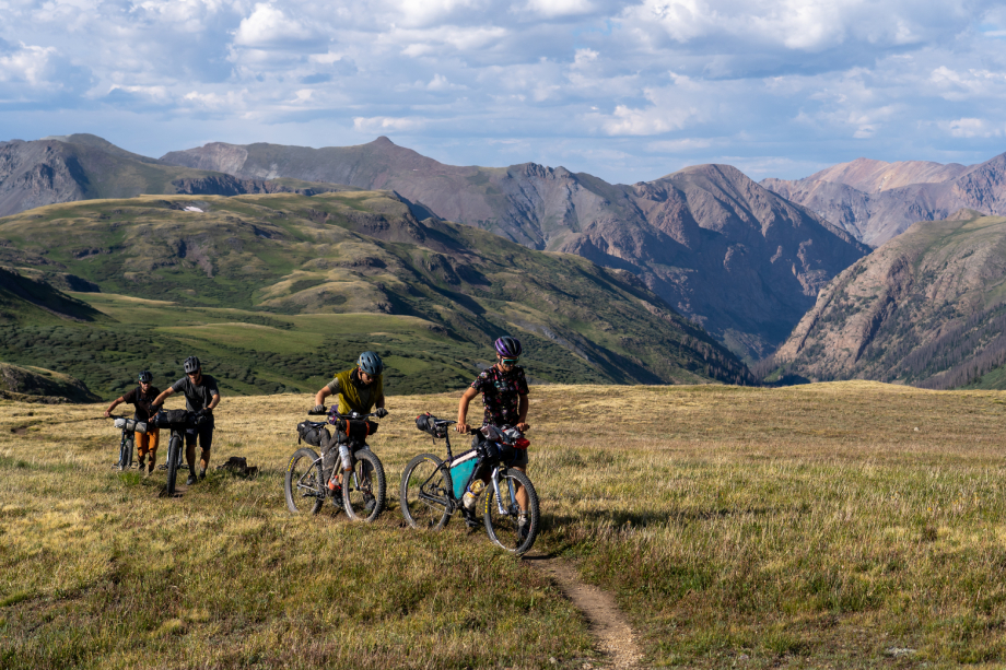 Behind the scenes shot of four men pushing their bikes up a grassy mountain from Kody Kohlman's film C-Team shot for Fat Tire