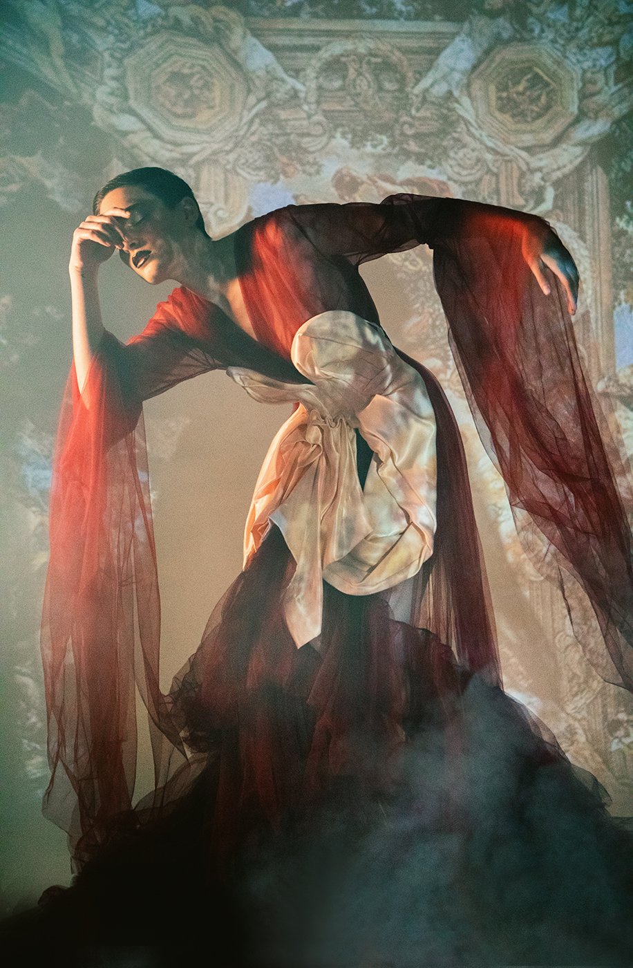 Model Amelia Pool draped in a red long sleeve toile gown in front of projected Renaissance art shot by Kirsten Miccoli