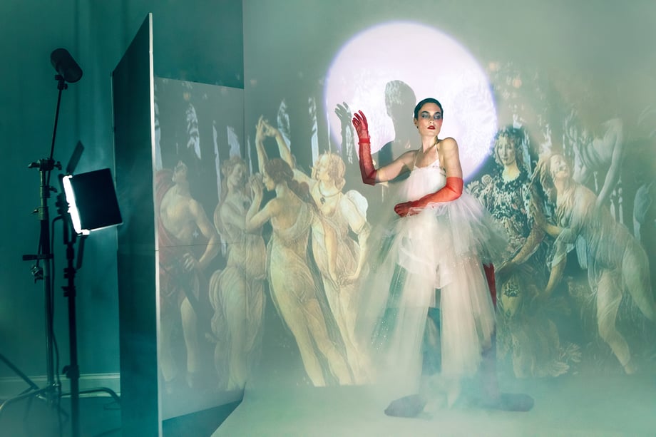 Model Amelia Pool wearing white toile dress and red gloves standing in front projected Renaissance art shot by Kirsten Miccoli