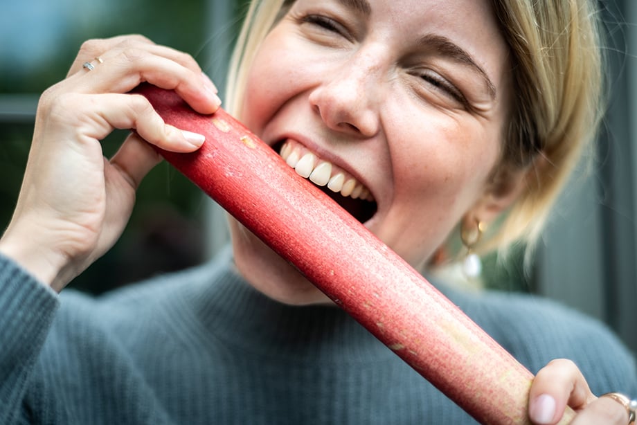 A playful shot of a woman pretending to eat a rhubarb stalk. Photography by Lola Akinmade. 