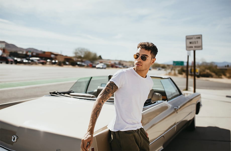 A male model poses in front of a Cadillac convertible on the road. Photographed by Marissa Roseillier for American Optical. 