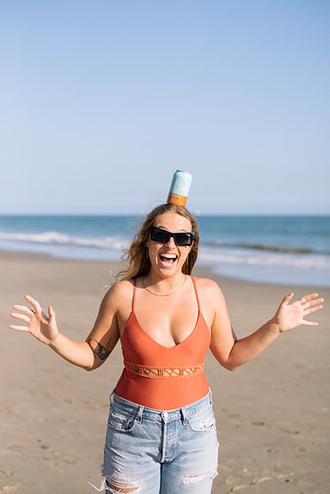 A model balances a can of Dos Topas on her head in a beach scene. Photographed by Mikaela Hamilton for Topa Topa Brewing.