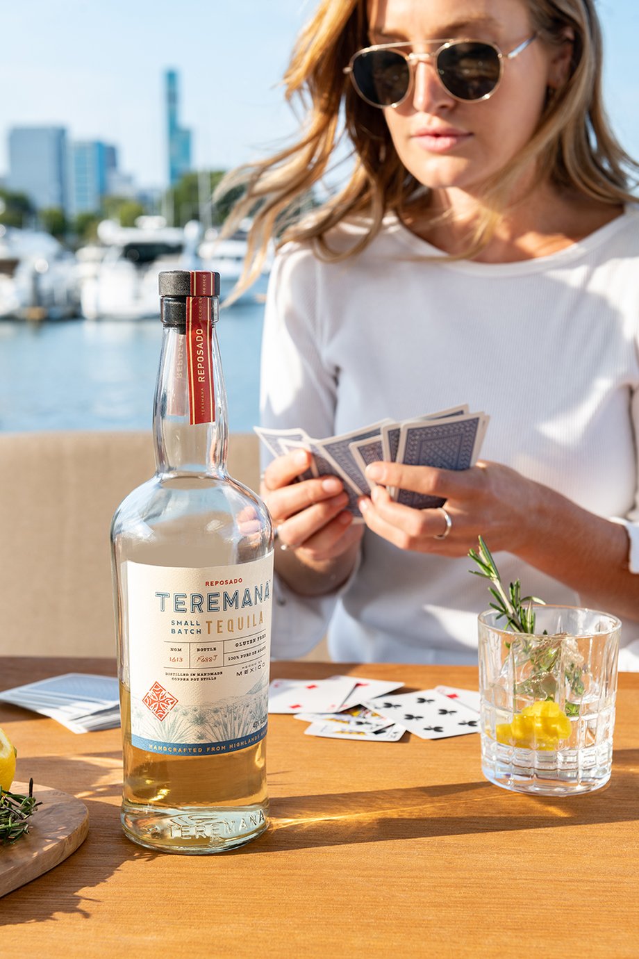 Woman playing cards on a boat with a near empty glass of Teramana Tequila garnished with citrus and rosemary shot by Morgan Ione