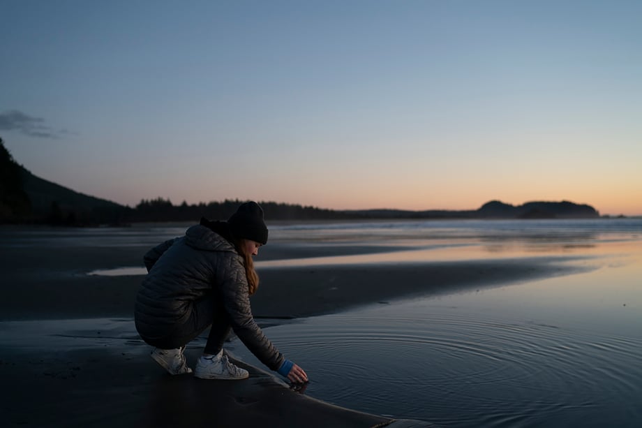 Young woman touching still waters on a cold Washington beach at sunset shot by Motofish for Hest.