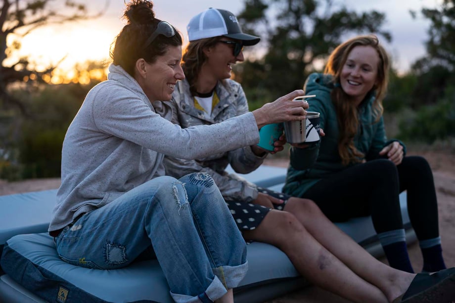 Three women clink cups while sitting on top of Hest mattress in Moab desert shot by Motofish