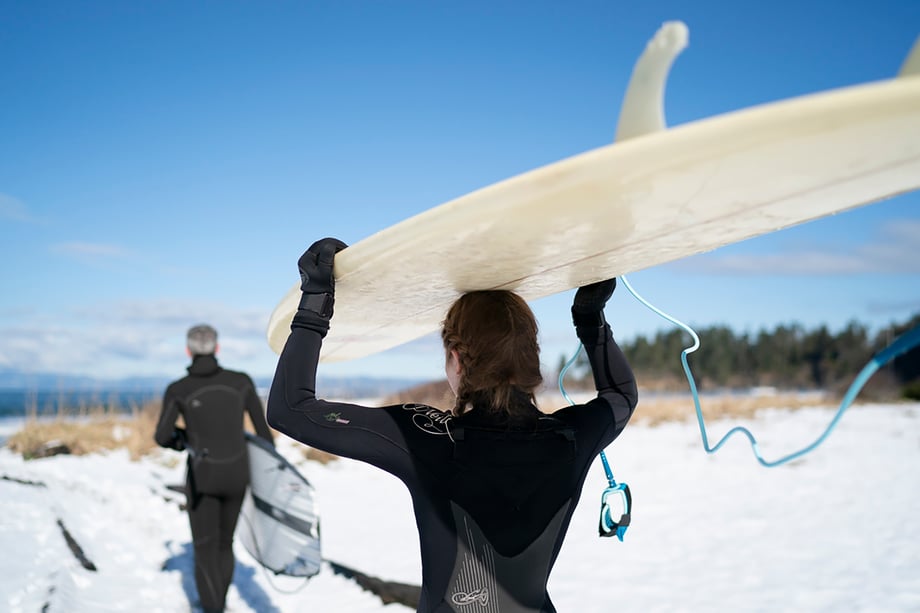 Father and daughter carry surfboards across a snowy beach in Washington shot by Motofish for Hest