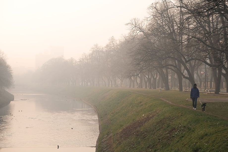 A man walks his dog along the banks of the Miljacka river on a heavily polluted evening in Sarajevo. Photography by Nick St. Oegger. 
