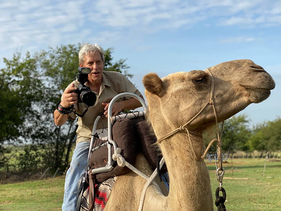 Scott Van Osdol riding a camel while taking photos.