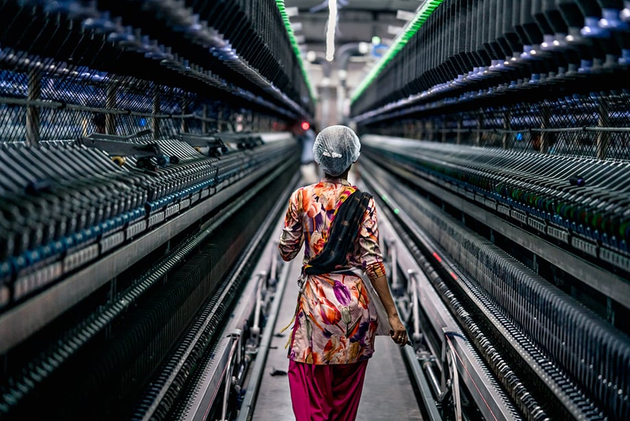 A factory worker in India walks through a line of textile machines. Photography by Tim Gerard Barker.