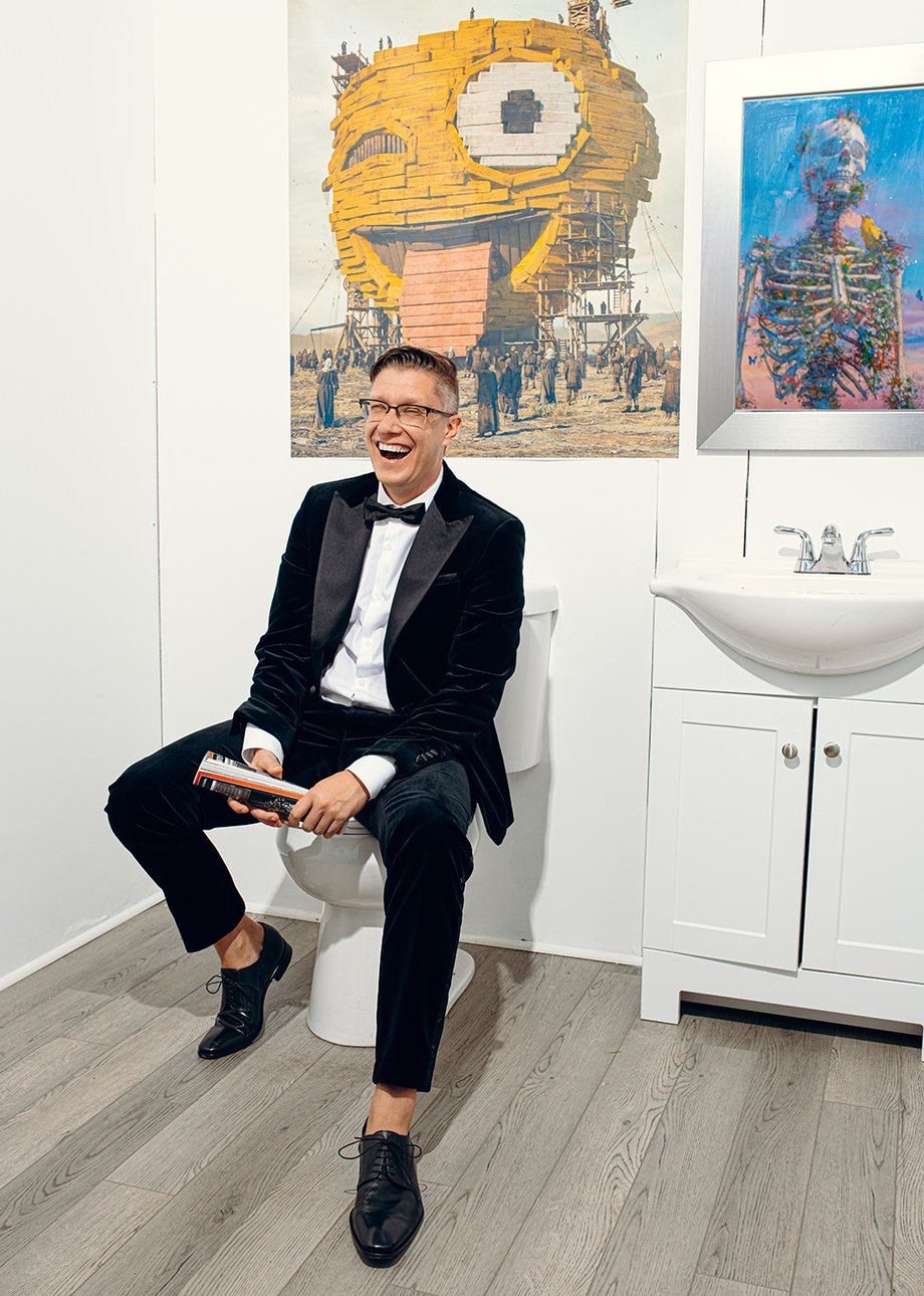 Beeple sitting on the toilet in his bathroom with his art on display behind shot by Will Crooks for British GQ