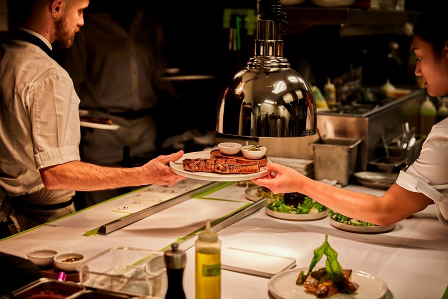 A chef places finishing touches on a dish and passes it to waitstaff in this photo by Andrea D'Agosto