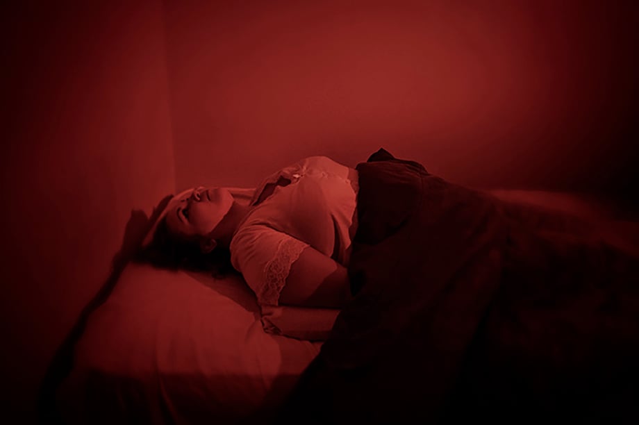 Woman lies in bed with a red light to mimic the experience of being abducted for Annick Donkers' photobook Un-identified.