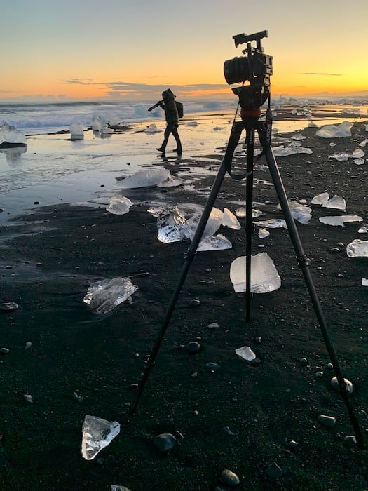 A behind the scenes shot of photographer and director Rachid Dahnoun carrying a tripod on the black sand beaches in Iceland.