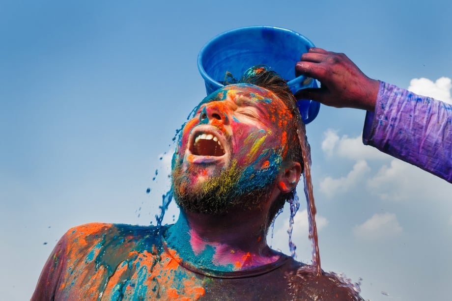 Portrait of subject, mouth open, as a blue bucket of colorful liquid is poured over his head, by Mumbai-based portrait photographer Parikshit Rao.