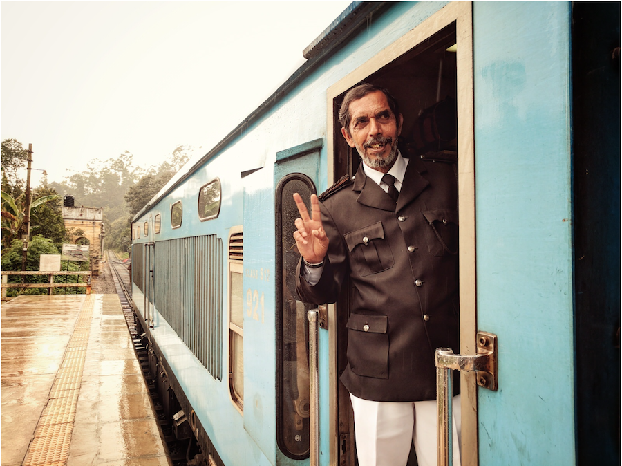 A man gives a peace sign as he stands in the doors of a bright blue train my photographer Andreas Chudowski of Berlin Germany. 