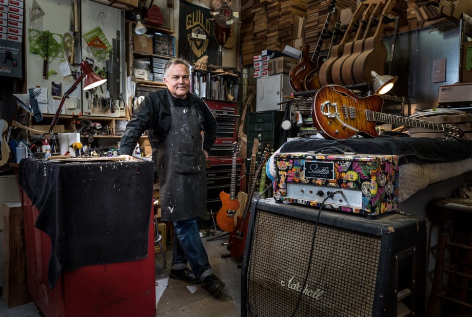 A man posing in a guitar and amo repair workshop. Creative in Place Carry a Tune photographer Bill Purcell, Olympia, Washington. 