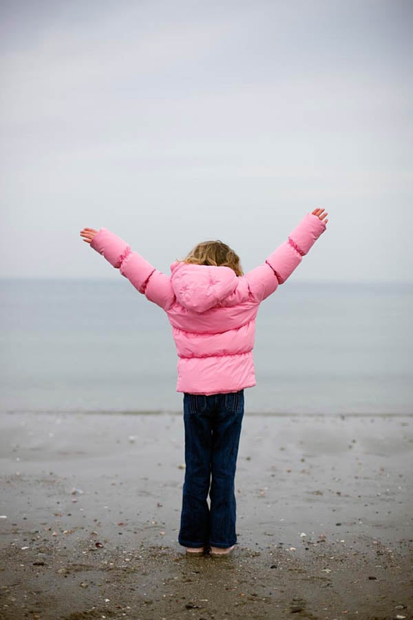 A little girl in a pink jacket raises up her arms in front of the sea by photographer Dan Bigelow of Ridgefield, Connecticut. 