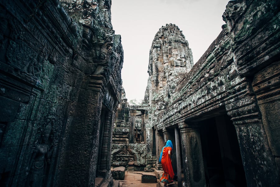 Muslim woman in orange dress and blue head scarf exploring the ruins of Angkor Wat by photographer Inti St. Clair