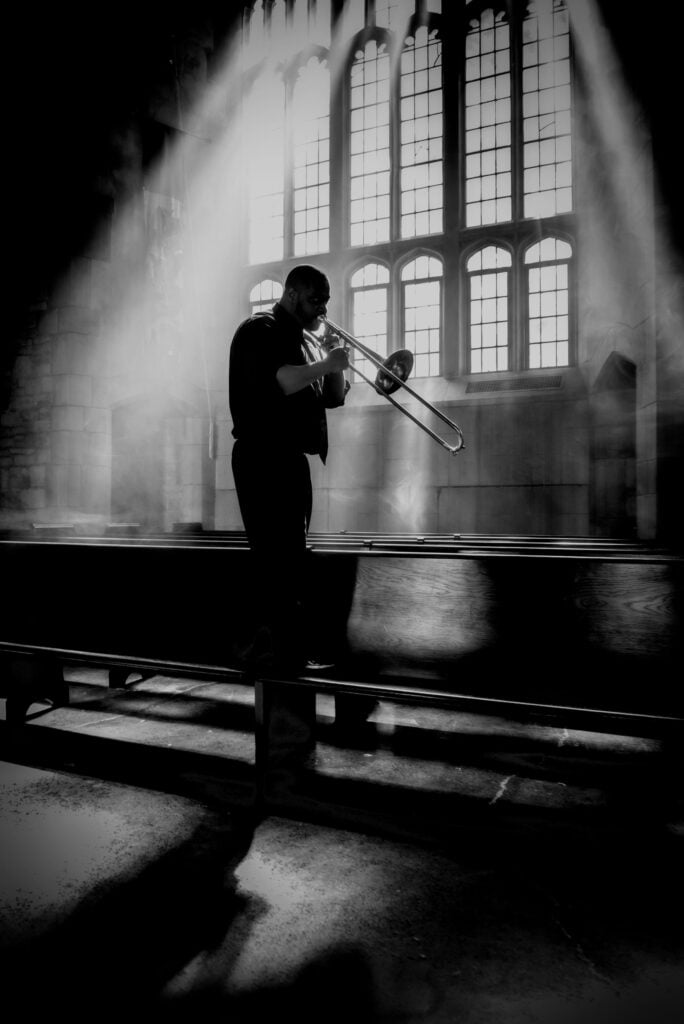 A man plays the trombone in a church. Creative in Place Carry a Tune photographer John Boehm, Chicago, Illinois