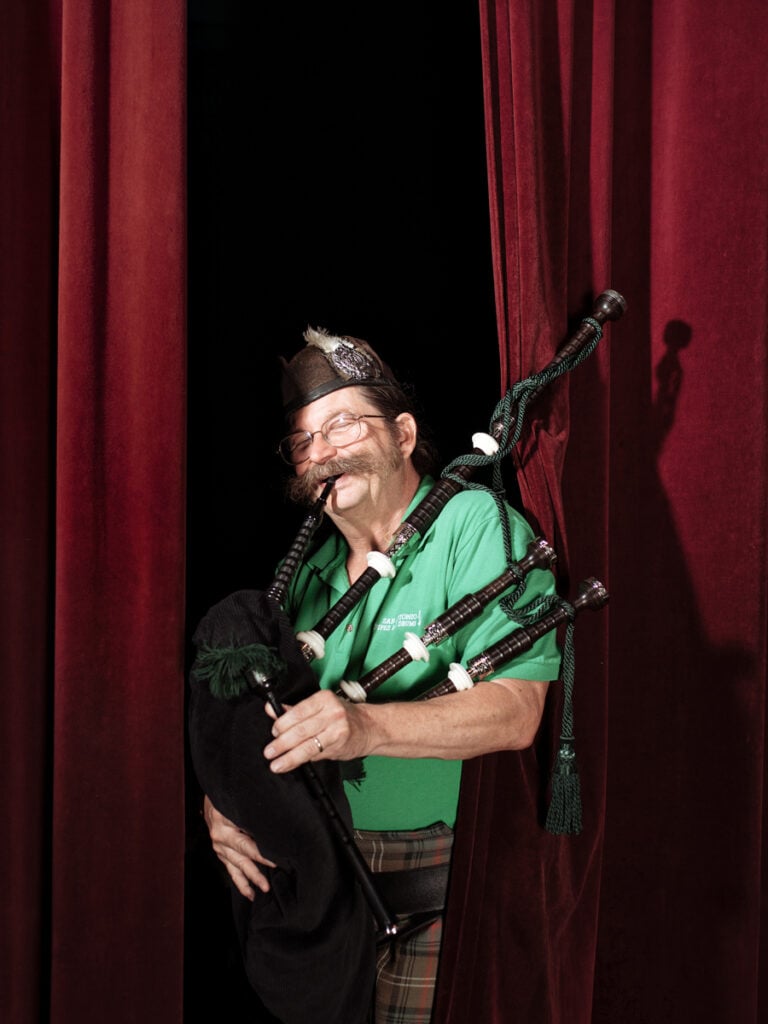A happy man plays the bagpipes as he peeks behind a curtain. Creative in Place Carry a Tune photographer Josh Huskin, San Antonio, Texas