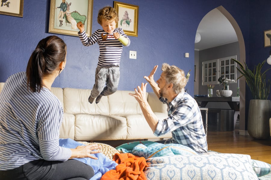 A young boy jumps off of a couch into his parents' arms by photographer Leah Fasten of Falmouth, Massachusetts