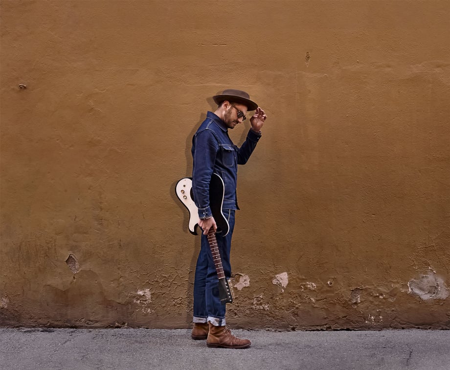 Photo of a musician holding a guitar and tipping his hat