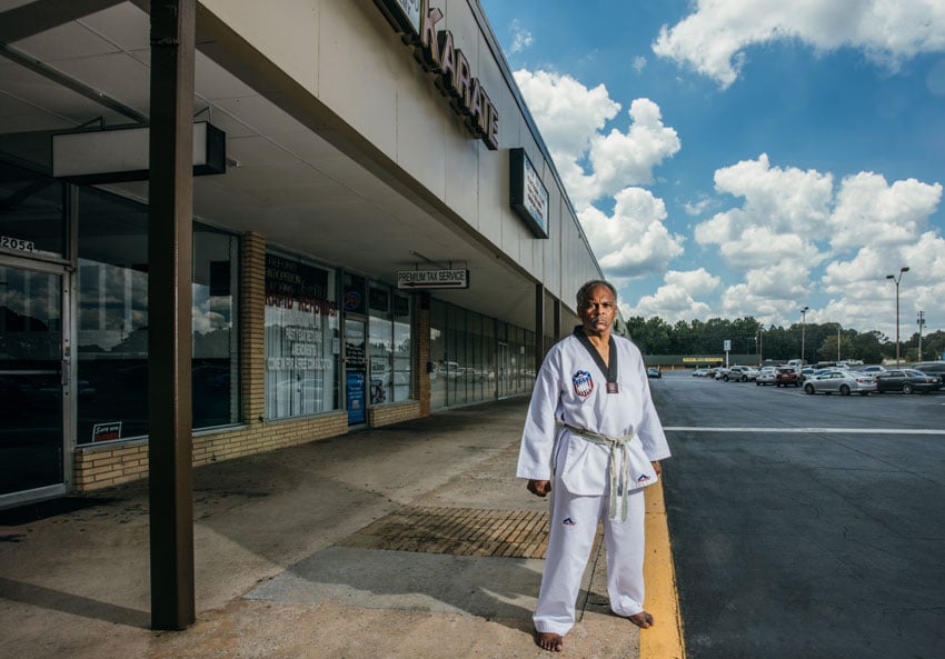 Black small business owner Isaac Thomas stands barefoot on the curb outside his studio in Matt Odom's photo for Bloomberg 