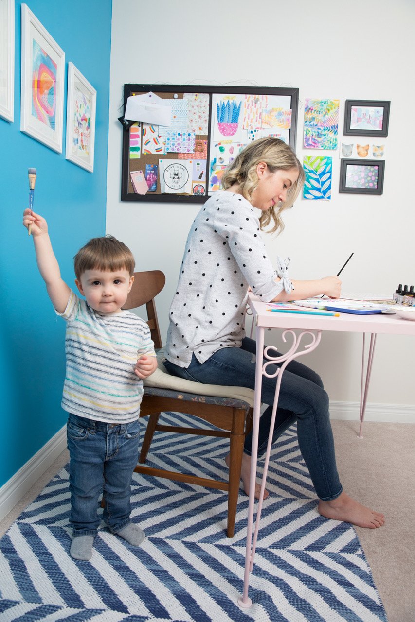 Michelle Gibson photographs Sara Funduk at work with her son playing in the forefront for Playing with Paints