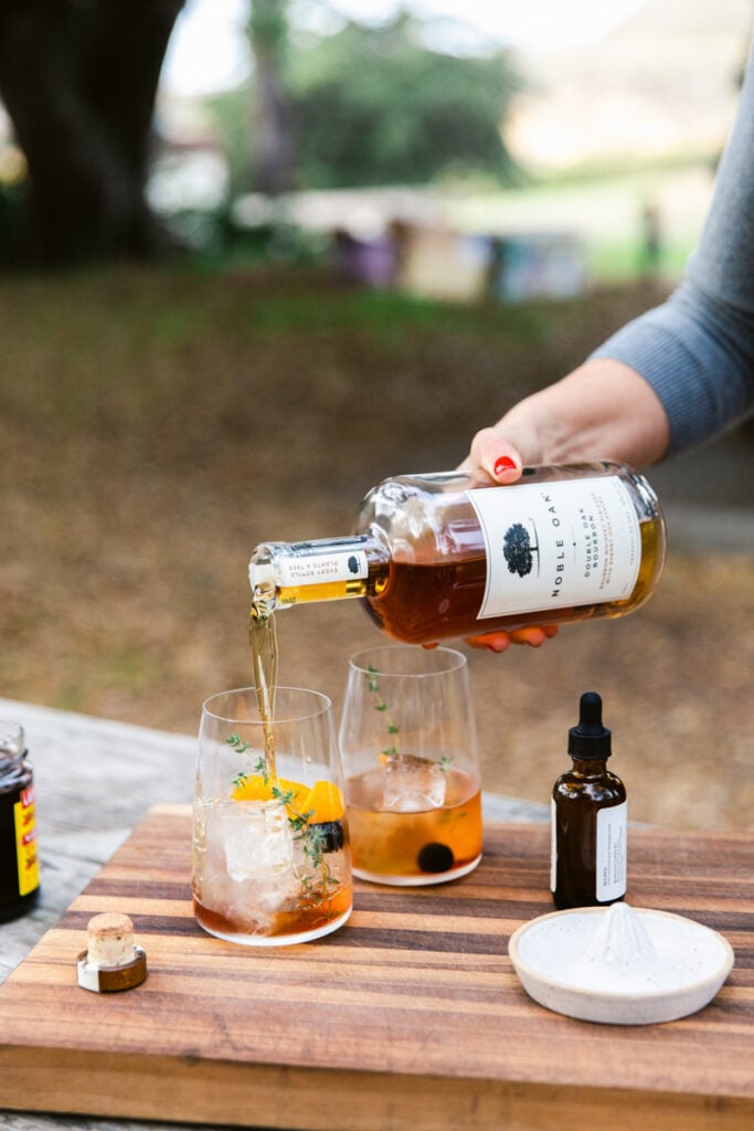 A woman pours Noble Oak bourbon into two cocktail glasses