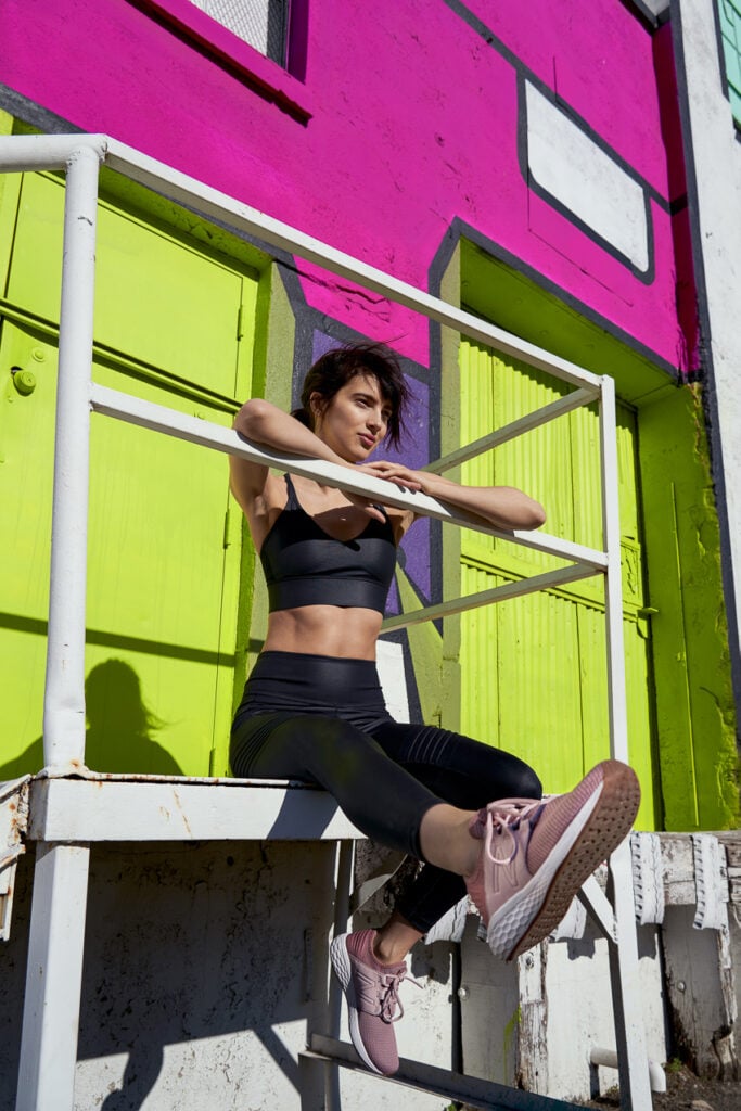 Photo of a woman sitting at the top of a short stairway leading to an entrance to a bright green colored warehouse a New Balance campaign with VML agency. 